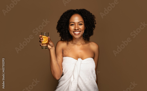 Cheerful half-naked black woman holding glass with orange water