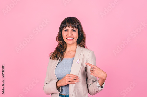 Smiling woman wearing a pink breast cancer awareness ribbon while pointing at it.
