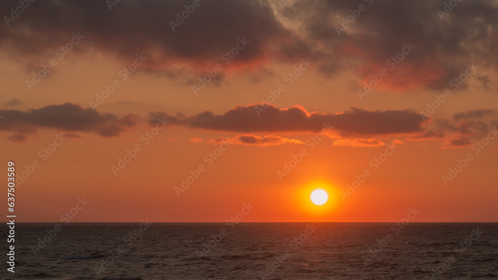 Sunrise from behind the horizon over the seas golden water and sky.