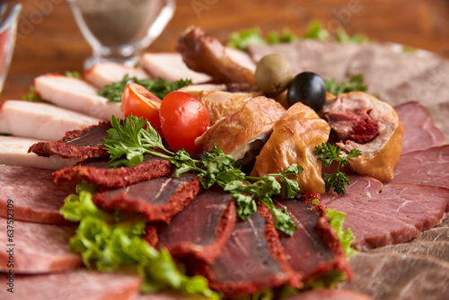 Part of plate with cold cuts with choice - salami, pieces of sliced ham, sausage, chicken, qazi horse meat, tomatoes on salad, close-up, shallow depth of field