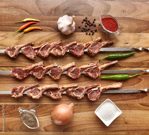 Metal skewers with raw uncooked lamb meat for frying on the wooden board with chili peppers, garlic and onion, spices and salt near it, top view flatlay
