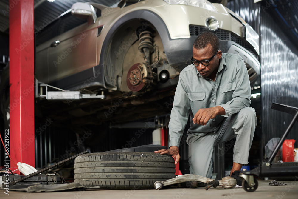 Serious mechanic in grey overall checking car tire