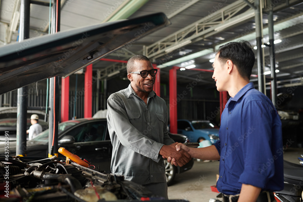 Positive mechanic shaking hand of owner of car that needs to be repaired Positive mechanic shaking hand of owner of car that needs to be repaired