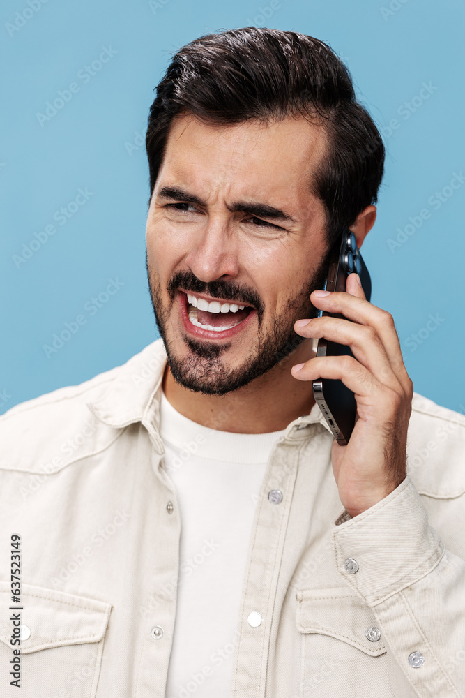 Portrait of male brunette anger talking on the phone in close-up, disgruntled, on a blue background in a white T-shirt and jeans, copy space Portrait of male brunette anger talking on the phone in close-up, disgruntled, on a blue background in a white T-shirt and jeans, copy space