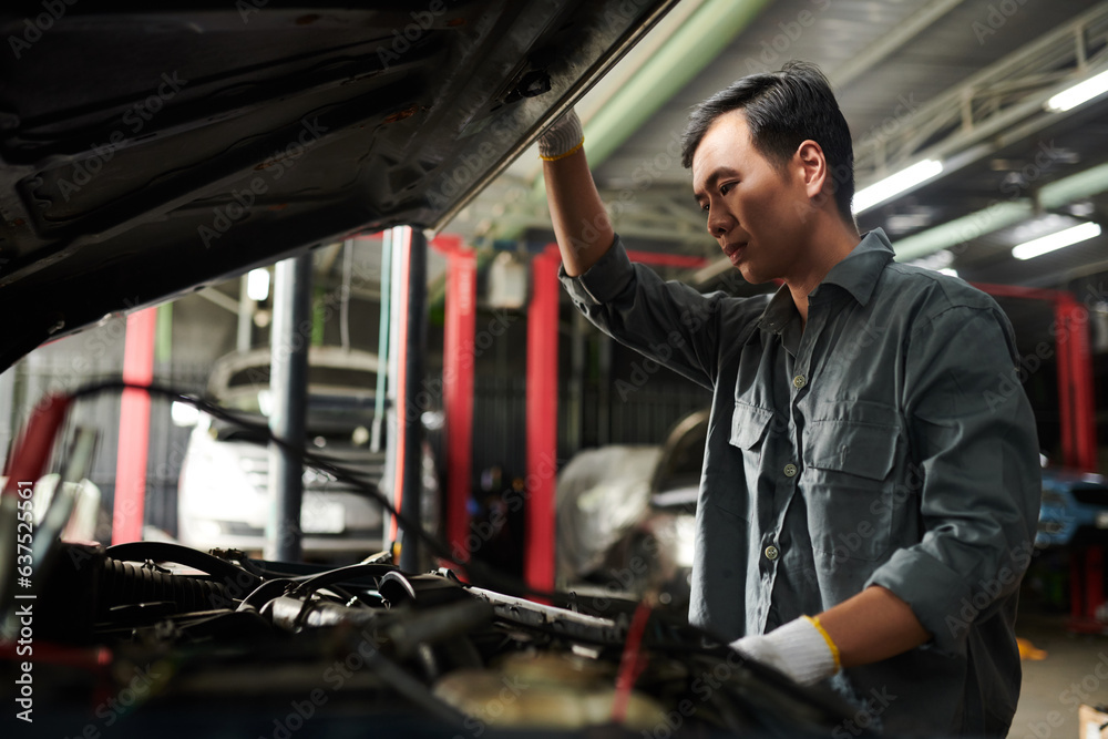 Pensive mechanic opening car hood to check engine