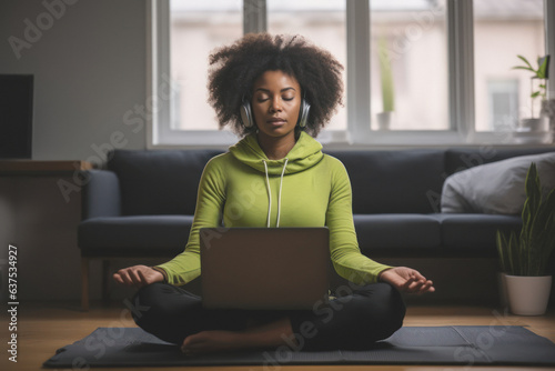 A young Afro-American woman learns to meditate in a guided session by an online instructor through her laptop at home to enhance her mental health.