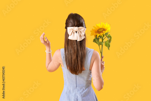 Young woman with beautiful sunflower on yellow background, back view
