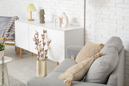 Interior of light living room with grey sofa, standard lamp and white sideboard