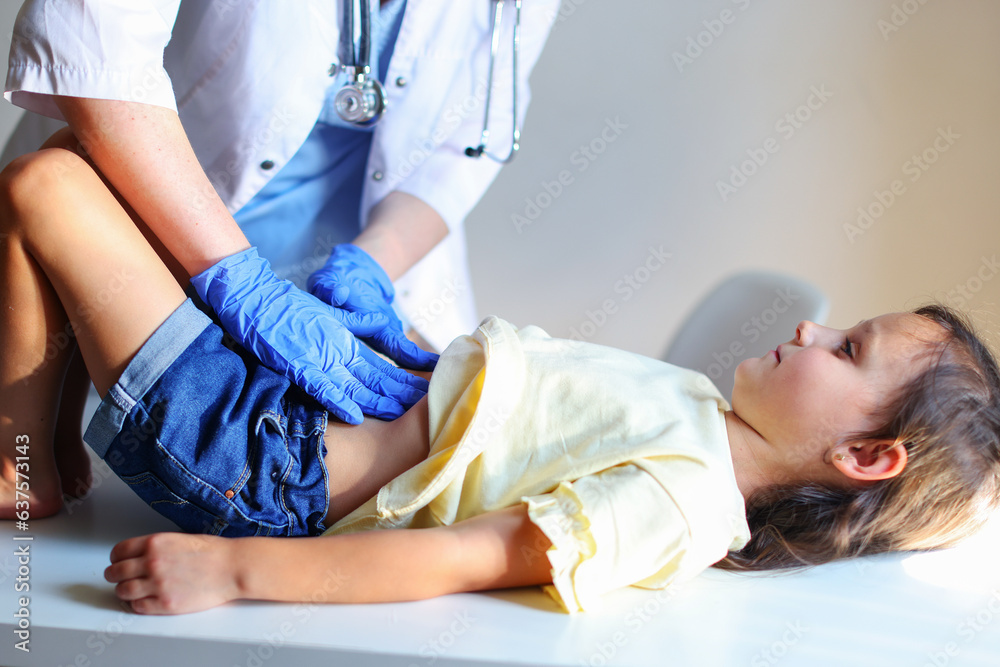 Obraz premium Pediatrician is examining a school child on the couch. The doctor is checking the baby's belly. Healthy lifestyle. Copy space. 