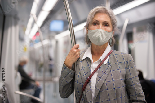 Mature woman in face mask standing inside subway train and waiting for next stop.