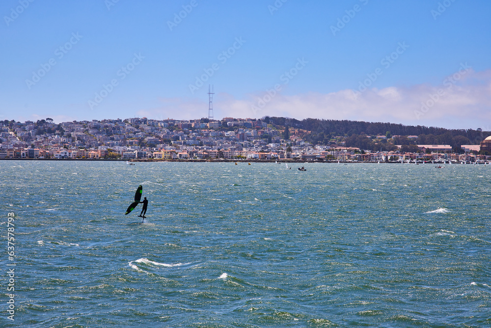 Man sailboarding on choppy bay waters with distant San Francisco shoreline
