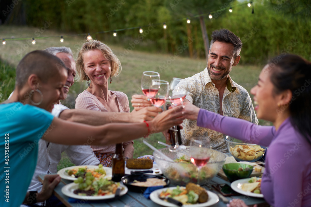 Group of middle-aged friends dining together on the terrace of a house or restaurant. Happy people eating and drinking toast at an outdoor table, sharing and enjoying time together. High quality photo