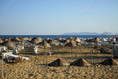 Fototapeta Naklejka Na Ścianę i Meble -  Große runde Sonnenschirme aus Korbgeflecht vor blauem Himmel im Licht der Abendsonne im Sommer am Strand von Sarimsakli bei Ayvalik in der Provinz Balikesir in der Türkei