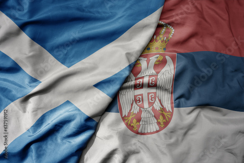 big waving national colorful flag of scotland and national flag of serbia .