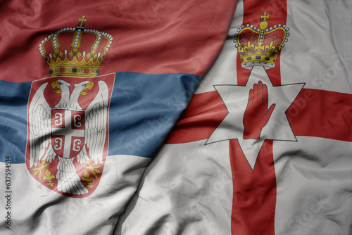 big waving national colorful flag of serbia and national flag of northern ireland .