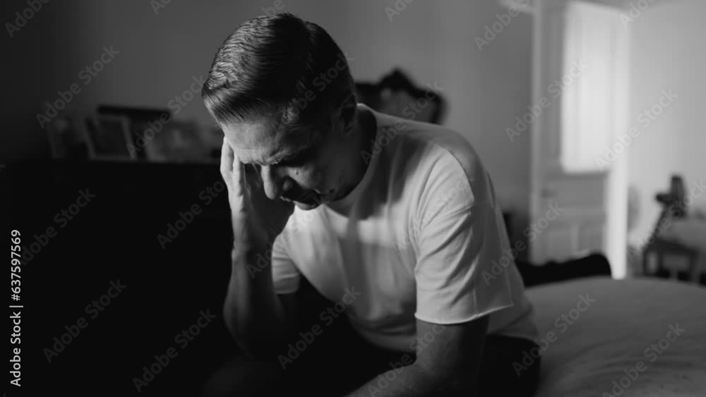 Dramatic Despair of middle aged man covering face in shame suffering alone in solitude, monochrome black and white while sitting by bedside, persons struggles with mental illness Dramatic Despair of middle aged man covering face in shame suffering alone in solitude, monochrome black and white while sitting by bedside, persons struggles with mental illness