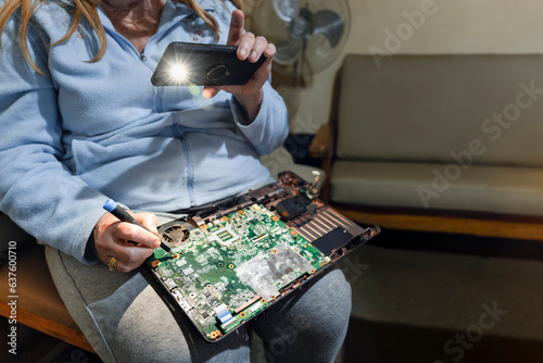 computer repairs, old woman in her seventies repairing her laptop, holding the phone light to see better