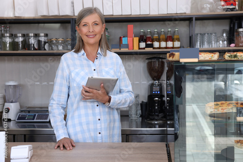 Happy business owner with tablet at cashier desk in her cafe