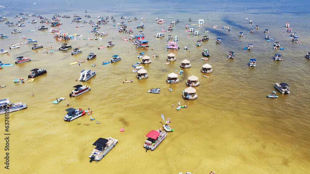 Crowd of people at Crab Island in Destin, Florida during low tide with brown brackish water, busy pontoons, jet skis, paddleboards, swimming, wading activities at shallow water
