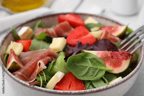 Tasty salad with brie cheese, prosciutto, strawberries and figs in bowl, closeup