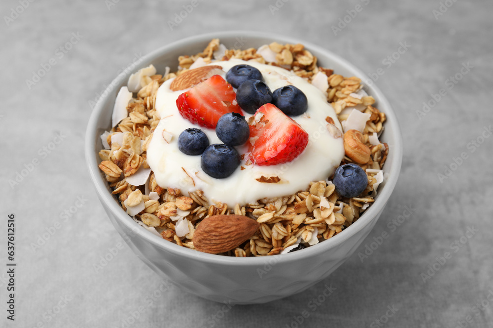 Tasty granola, yogurt and fresh berries in bowl on light grey table, closeup. Healthy breakfast