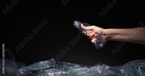 Waste reduction. Plastic recycling. Woman volunteer hand crushing used bottle throwing into trash dump with cellophane bags isolated on black background empty space.