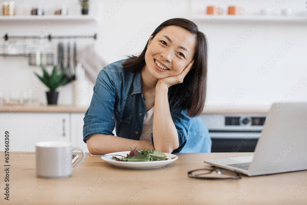 Remote employee sitting at table with laptop and salad Remote employee sitting at table with laptop and salad