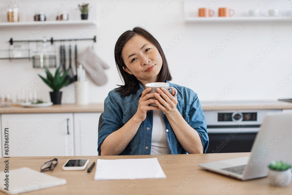 Adult posing with drink while working on laptop in kitchen Adult posing with drink while working on laptop in kitchen