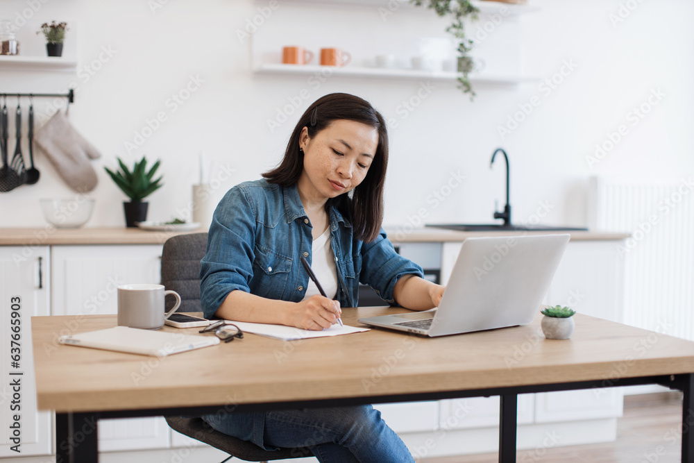 Adult writing down on paper while sitting behind laptop Adult writing down on paper while sitting behind laptop