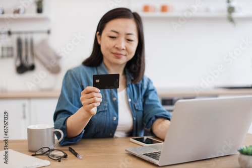 Lady staring at debit card while surfing net on laptop