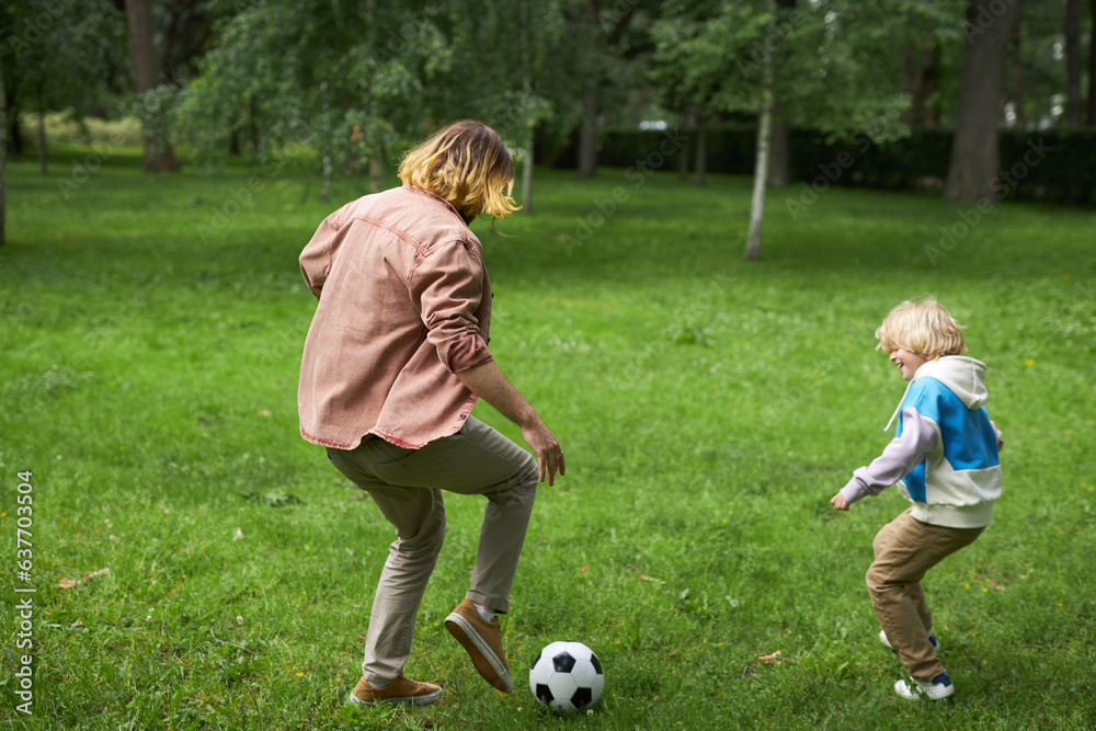 Action back view of father and son playing football together in green park, copy space Action back view of father and son playing football together in green park, copy space