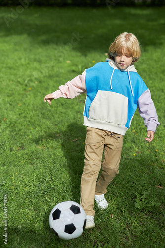 Vertical portrait of active tween boy playing football on green grass in sunlight