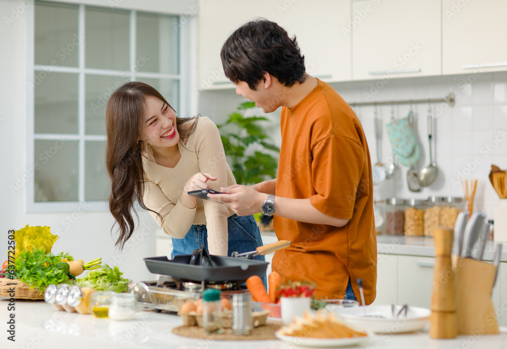 Asian young lovely lover couple husband and wife in casual outfit standing smiling holding touchscreen tablet computer learning helping cooking in full decorated modern kitchen with equipment at home Asian young lovely lover couple husband and wife in casual outfit standing smiling holding touchscreen tablet computer learning helping cooking in full decorated modern kitchen with equipment at home