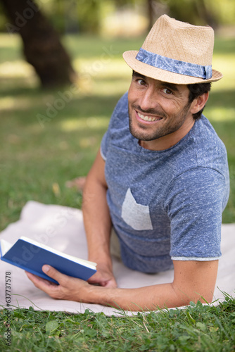 man smilling lying down in park reading a book