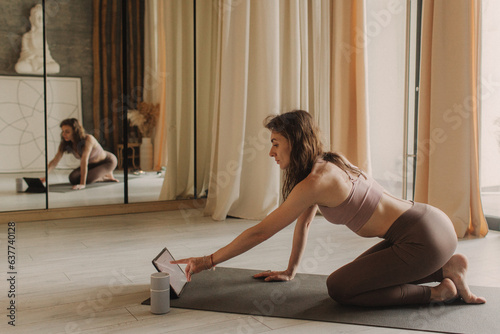 Young woman in sportswear exercises doing work out and using tablet to watch yoga video tutorial. Distant training with personal trainer, social distance, online concept. Soft focus and noise effect