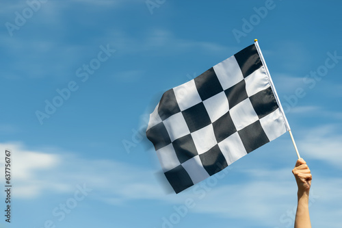 Checkered race flag in hand against blue sky © xy