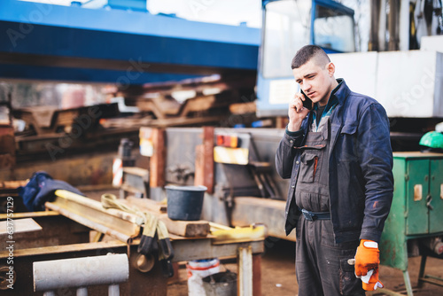 Slika na platnu Manual worker talking on mobile phone in shipyard construction site