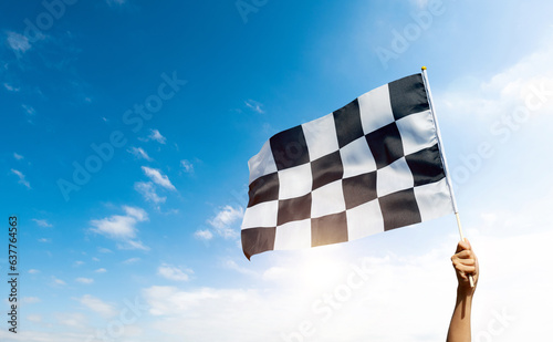 Checkered race flag in hand against blue sky