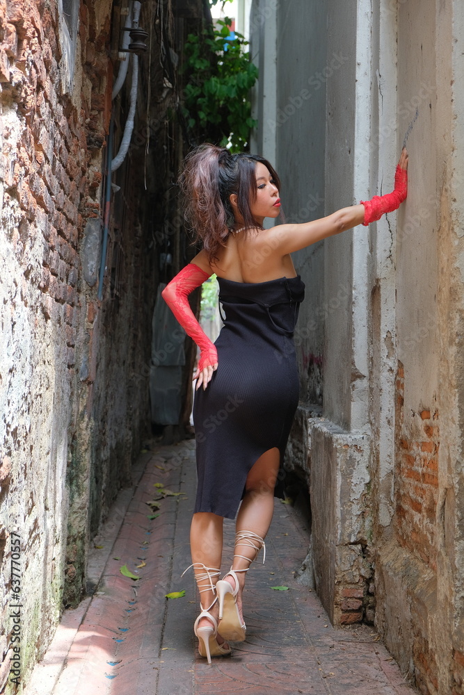 Asian woman stands in a small alley with hand on a wall
