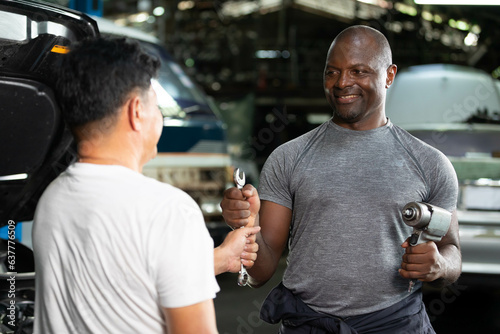 mechanic giving wrench to coworker for fixing a car in automobile repair shop