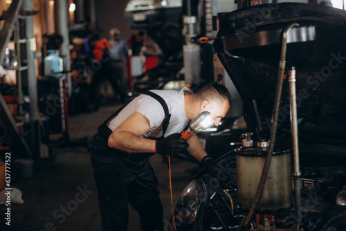 car service, repair, maintenance and people concept - auto mechanic man with lamp working at workshop