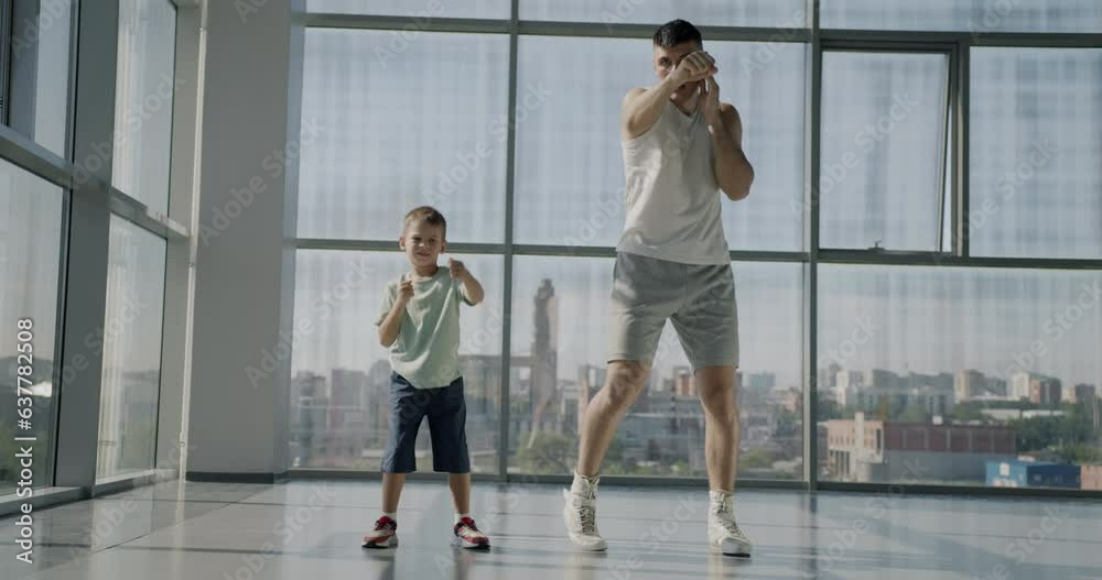 Slow motion portrait of adult man and little boy working out in gym together practicing boxing moves. Father teaching son martial arts. Slow motion portrait of adult man and little boy working out in gym together practicing boxing moves. Father teaching son martial arts.