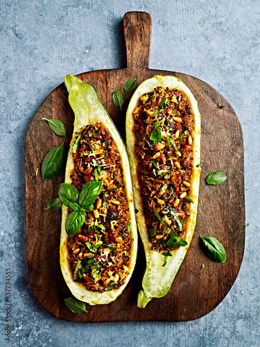 Oven baked zucchinis stuffed with minced meat, bulgur and vegetables; topped with olives, pine nuts and parmesan