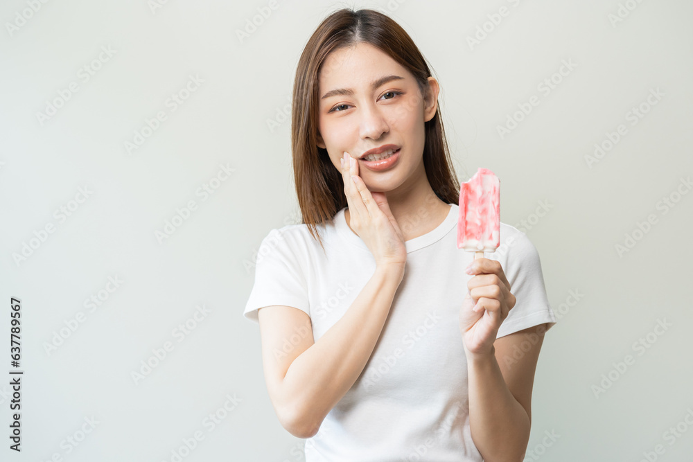 Face expression suffering from sensitive teeth and cold, asian young woman, girl hand touching her cheek, feeling hurt, pain eating ice cream, lolly. Toothache molar tooth at home, dental problem. Face expression suffering from sensitive teeth and cold, asian young woman, girl hand touching her cheek, feeling hurt, pain eating ice cream, lolly. Toothache molar tooth at home, dental problem.