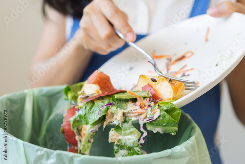 Compost from leftover food asian young housekeeper woman, female hand holding salad bowl use fork scraping waste, rotten vegetable throwing away into garbage, trash or bin. Environmentally responsible photo