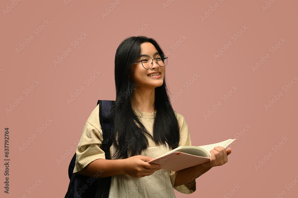 Teenager schoolgirl wearing glasses holding textbook over pink background. Educational, learning and back to school concept.