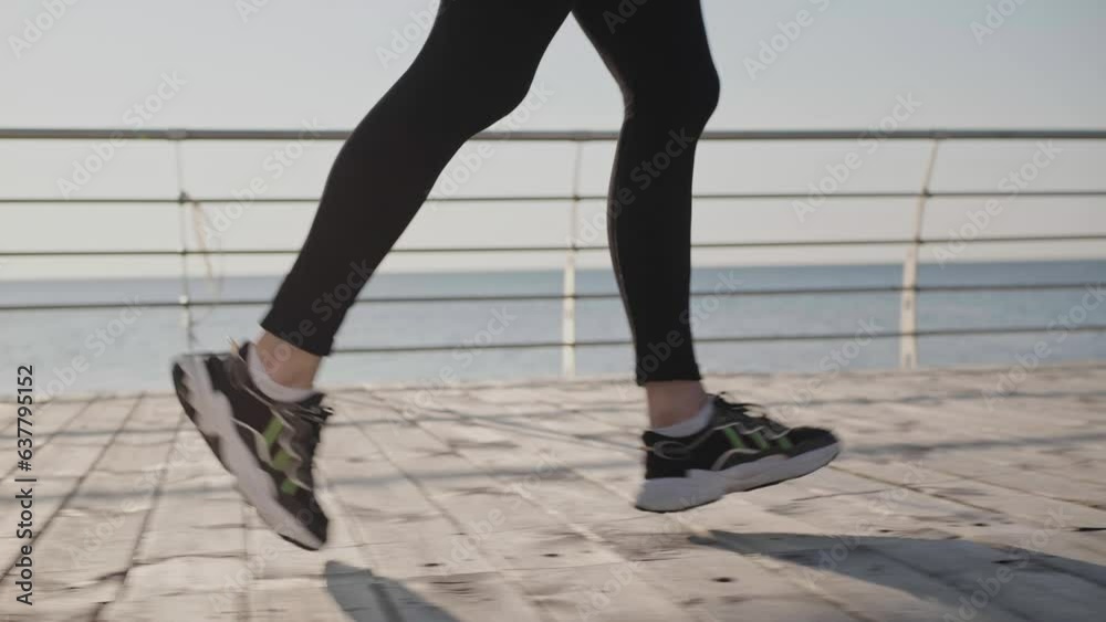Sporty young woman running on embankment near sea in morning, closeup. Camera moving with girl, slow motion effect Sporty young woman running on embankment near sea in morning, closeup. Camera moving with girl, slow motion effect