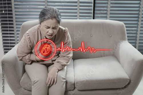 Asian senior woman sitting and suffering from chest pain or heart attack from working accident on sofa in living room.