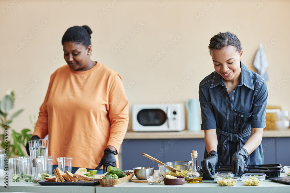 Portrait of two smiling African American women cooking together in kitchen and doing food prep at weekend