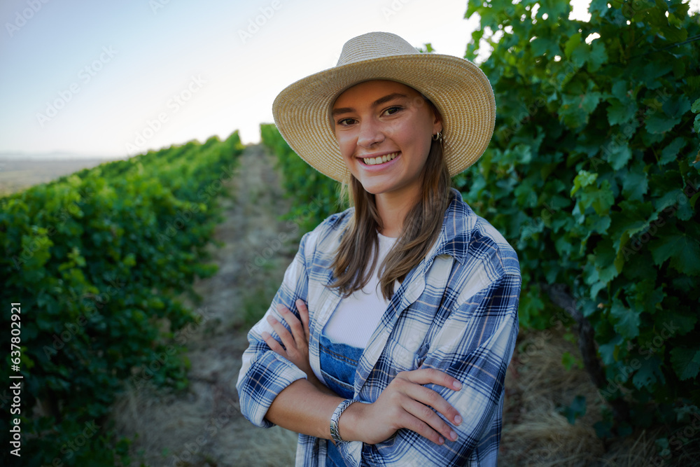 Happy young caucasian woman in checked shirt with arms crossed next to crops on farm